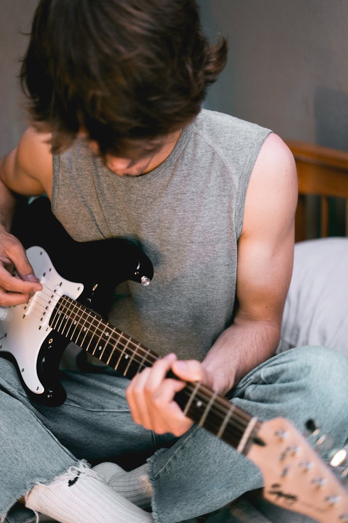 Casual young man in stylish attire playing an electric guitar indoors, showcasing creativity and relaxation.