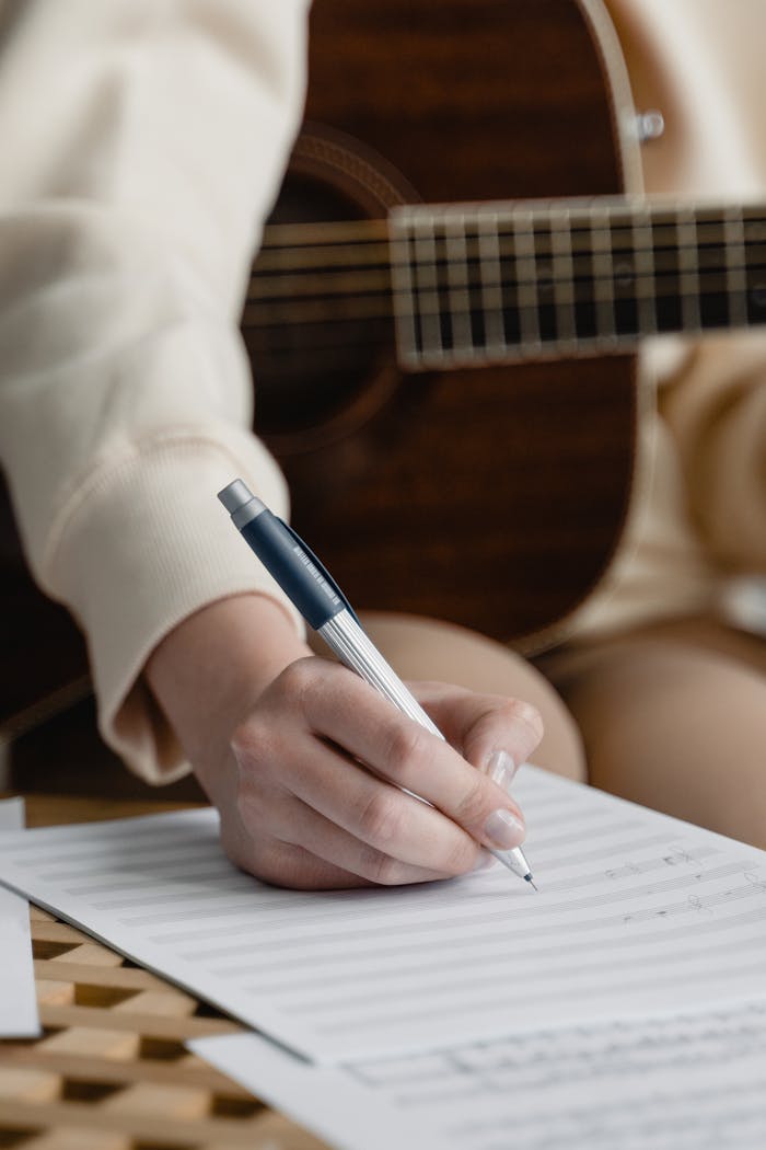 Close-up of a woman writing music notes with guitar in background.