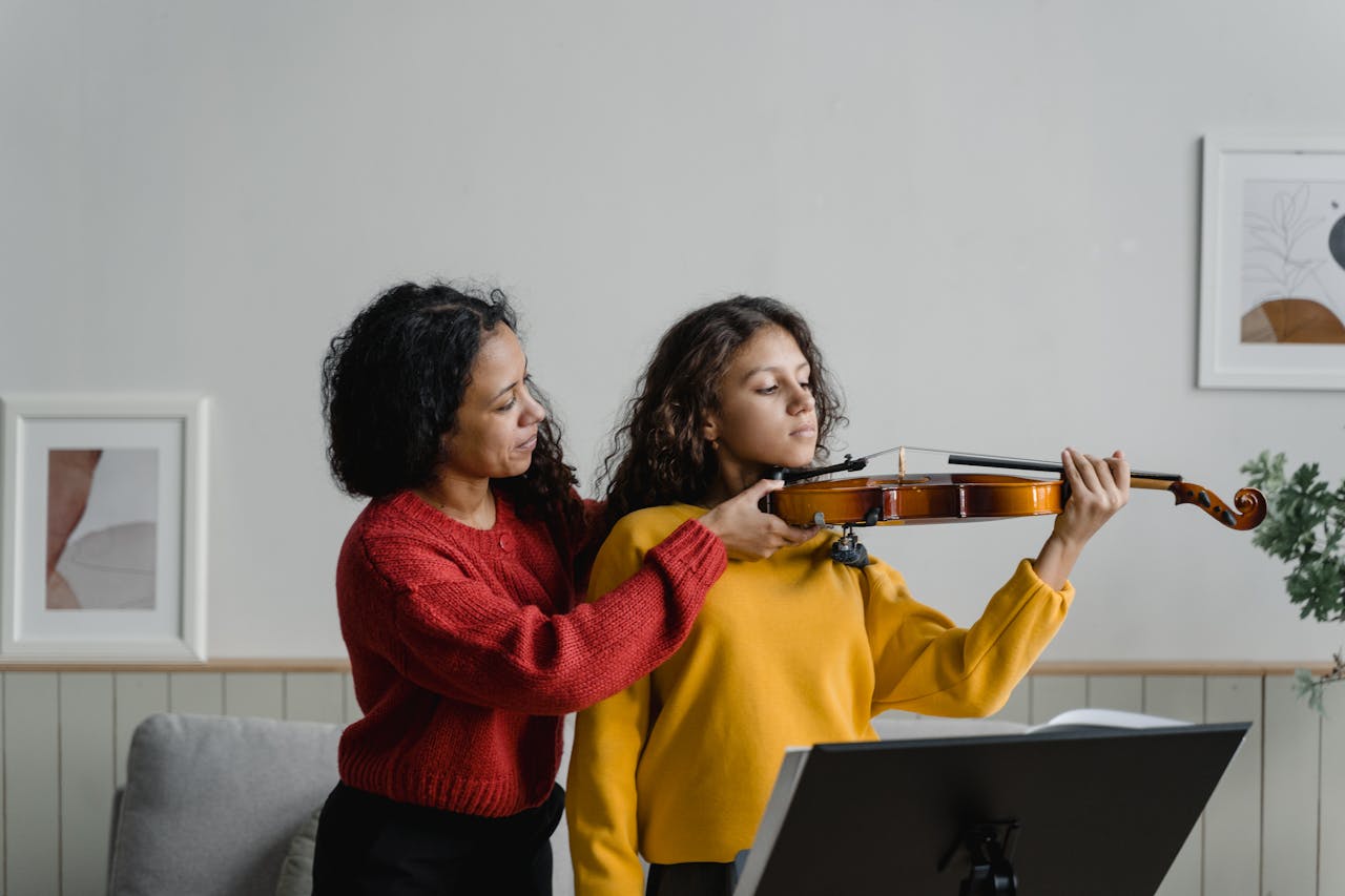 A woman teaches a young girl to play violin during a lesson at home, promoting music education.
